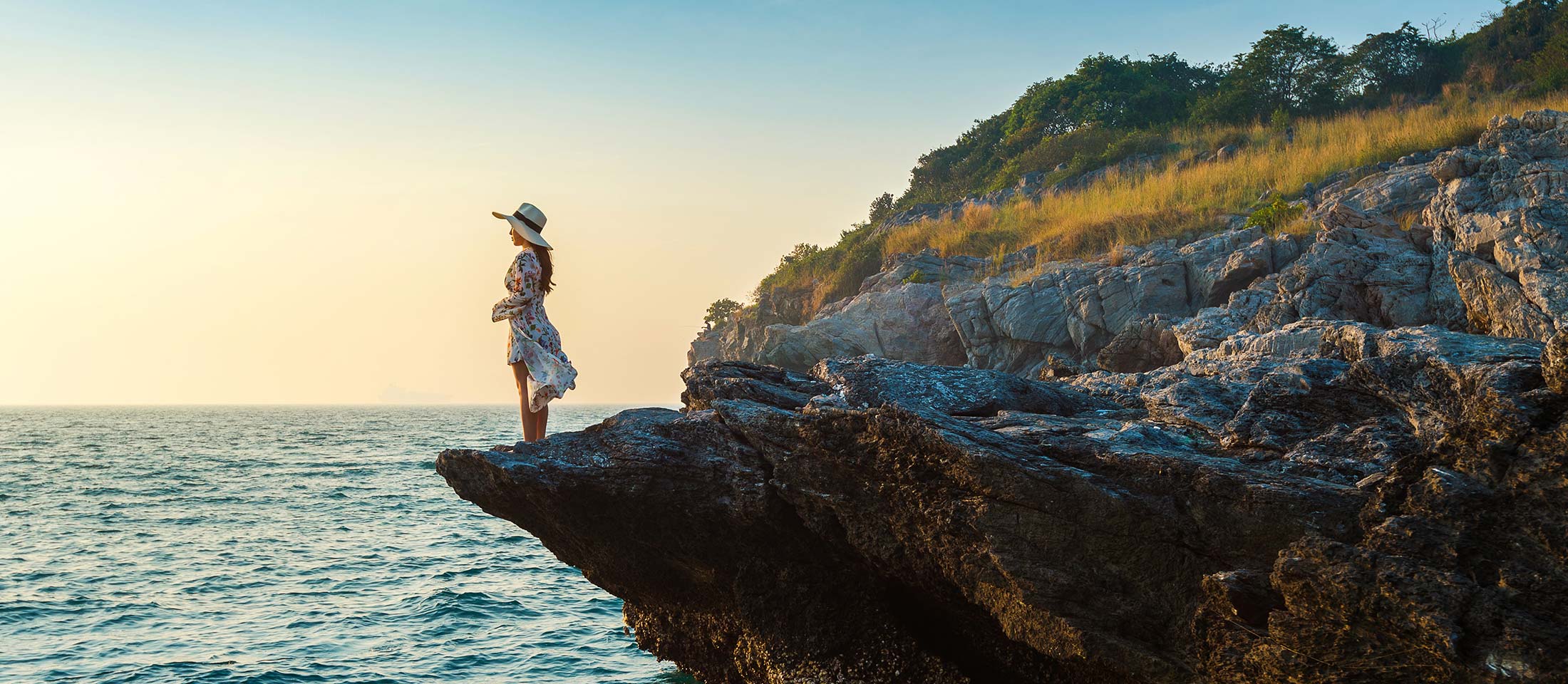 young woman standing top rock looking seashore sunset